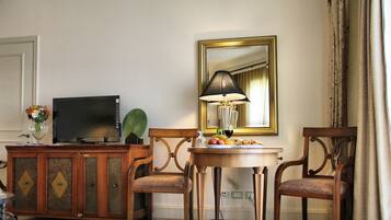 A hotel room with a wooden cabinet, a television, a table with fruit, a lamp, and a mirror.