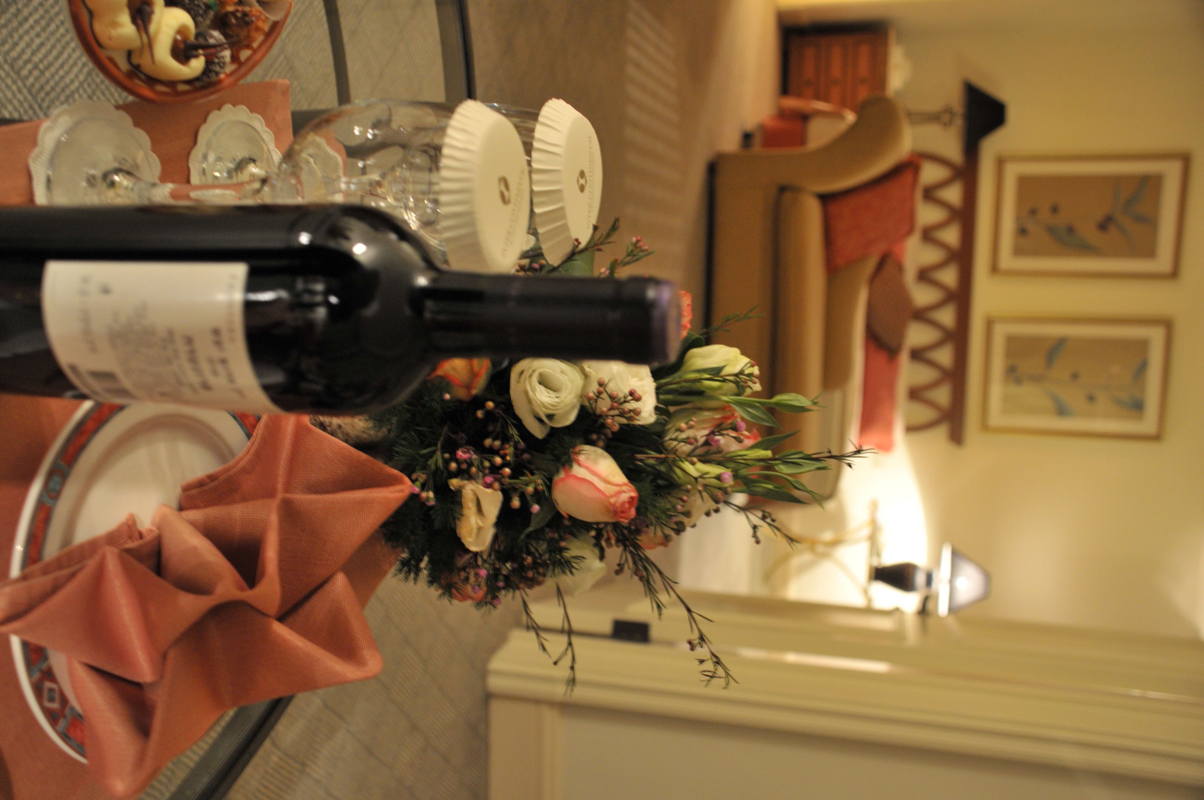 A table with a bottle of wine, a floral arrangement, and a folded napkin.