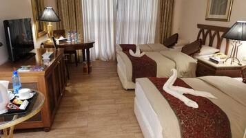 A hotel room with two beds, a desk with a lamp, a television, and a coffee table.