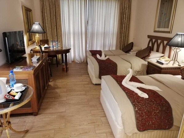 A hotel room with two beds, a desk with a lamp, a television, and a coffee table.