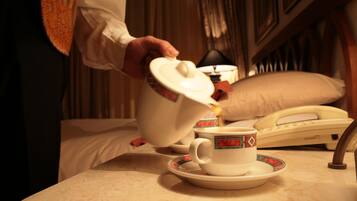 A person pouring tea into a cup on a table with a telephone and a pillow in the background.