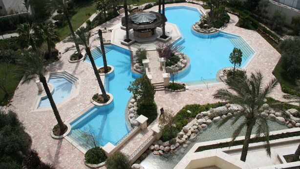A large outdoor swimming pool area with multiple pools, palm trees, and a gazebo. - Jacir Palace Hotel Bethlehem (Bethlehem)
