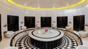 Ein luxuriöses Badezimmer mit einem zentralen runden Waschbecken, mehreren Spiegeln und einem Schachbrettmuster auf dem Boden.