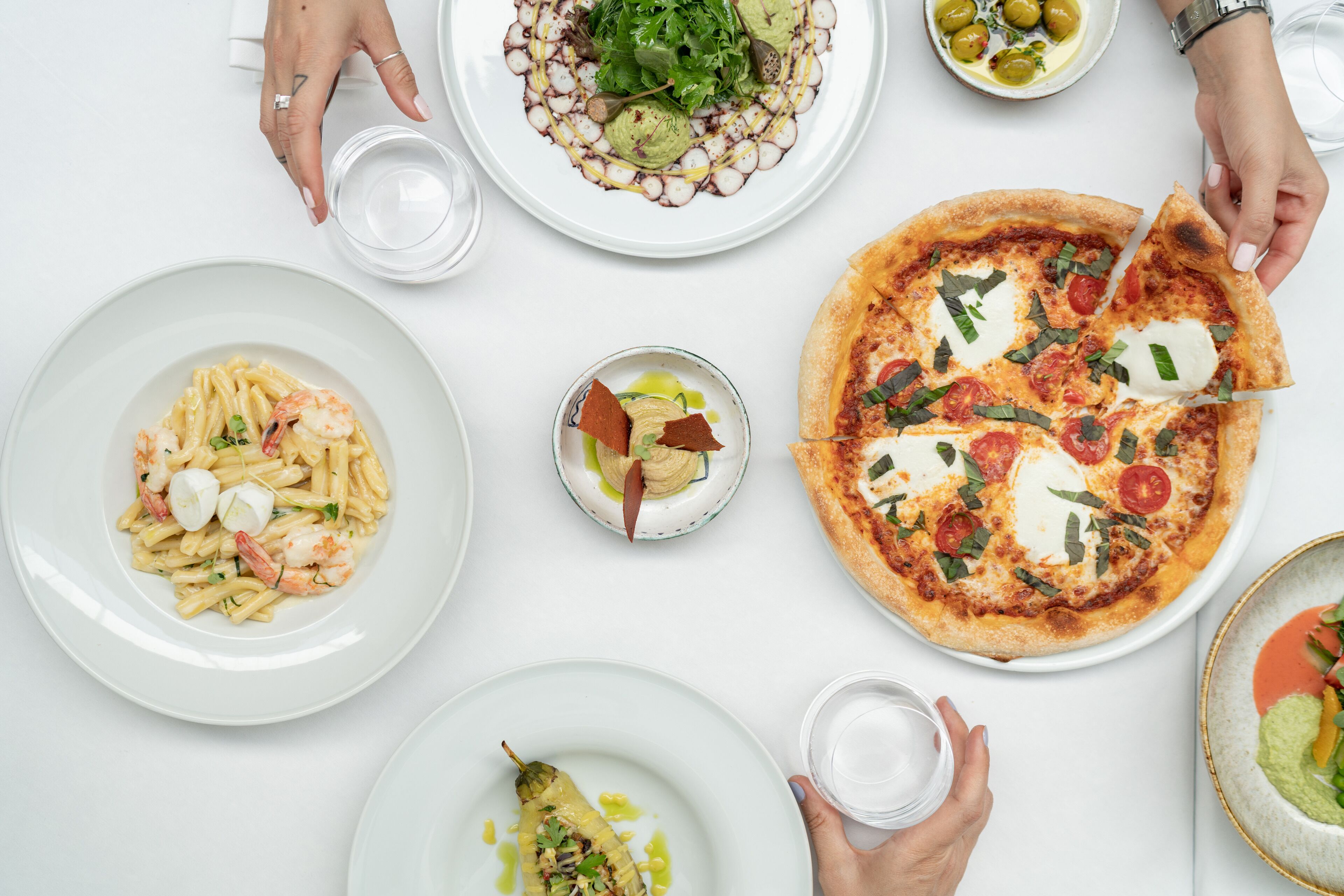 Een eettafel met diverse gerechten, waaronder pasta, pizza en een salade.