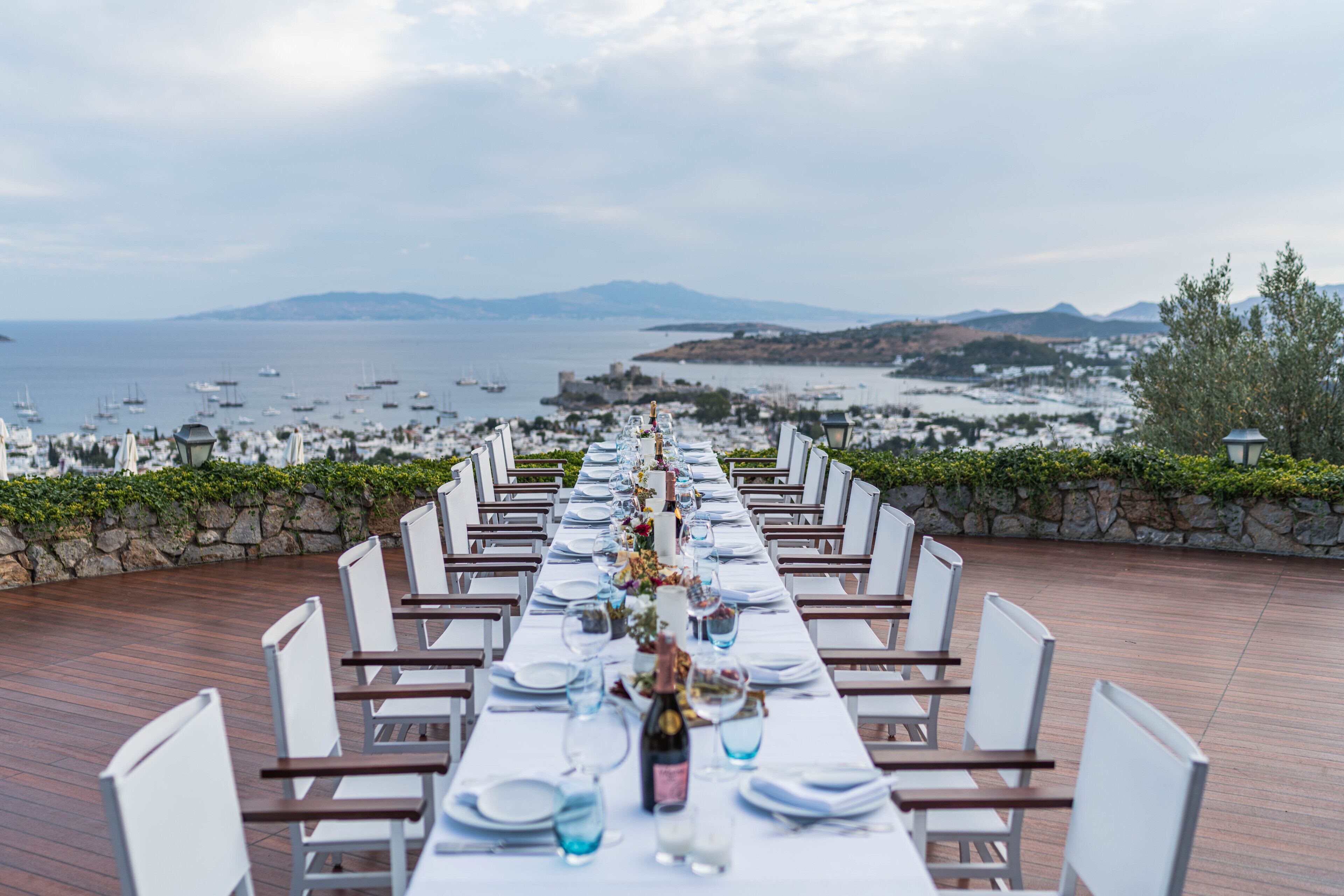 Una larga mesa de comedor dispuesta para una comida, con una vista panorámica del mar y las montañas al fondo.