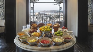 Ein reichhaltiges Frühstücksbuffet mit verschiedenen Früchten und Getränken, vor einer malerischen Kulisse einer Küstenstadt.
