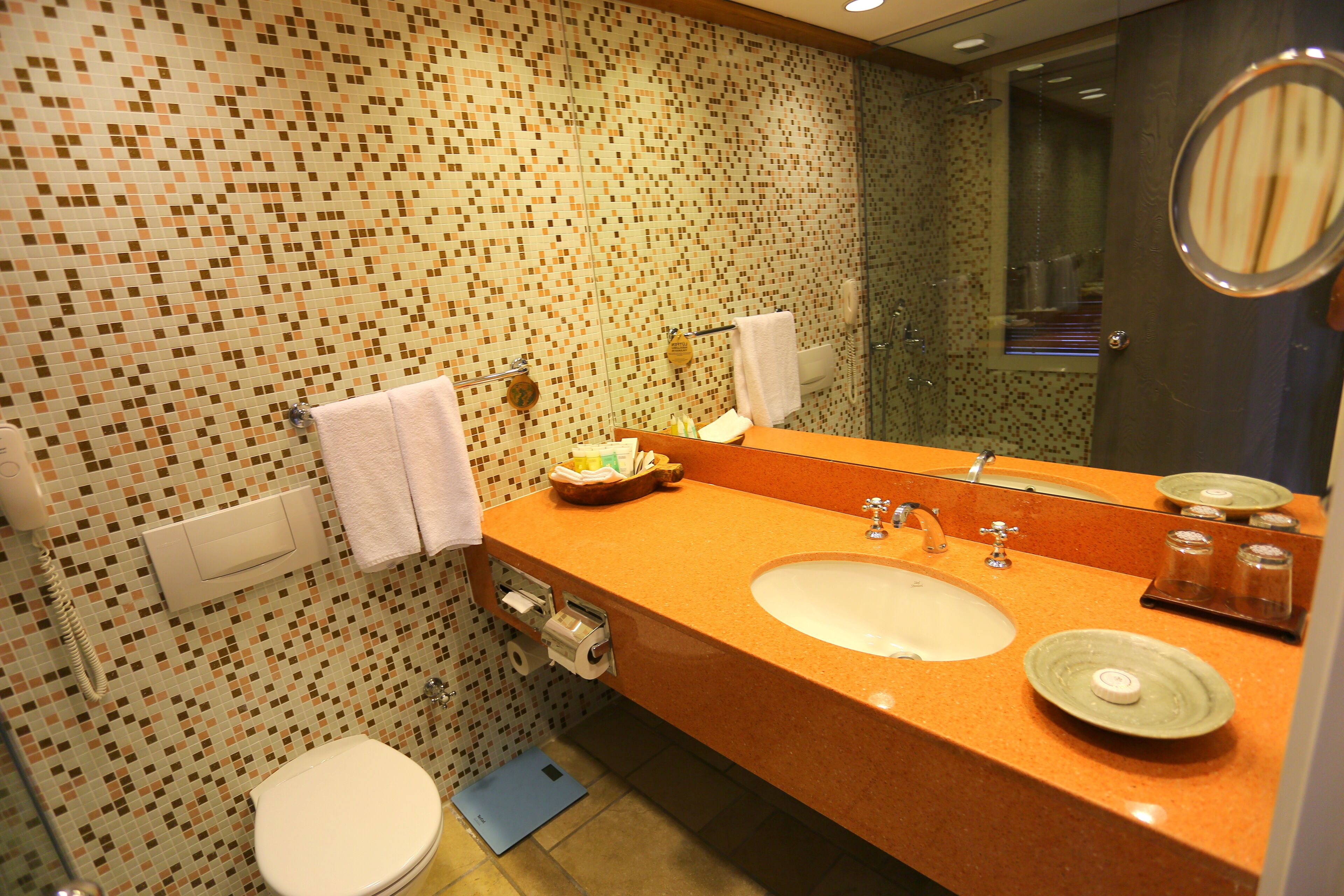 Une salle de bain avec un mur recouvert de mosaïques, deux lavabos, des toilettes et un miroir.