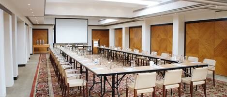 A conference room with a long table, chairs, a projector screen, and a patterned carpet.