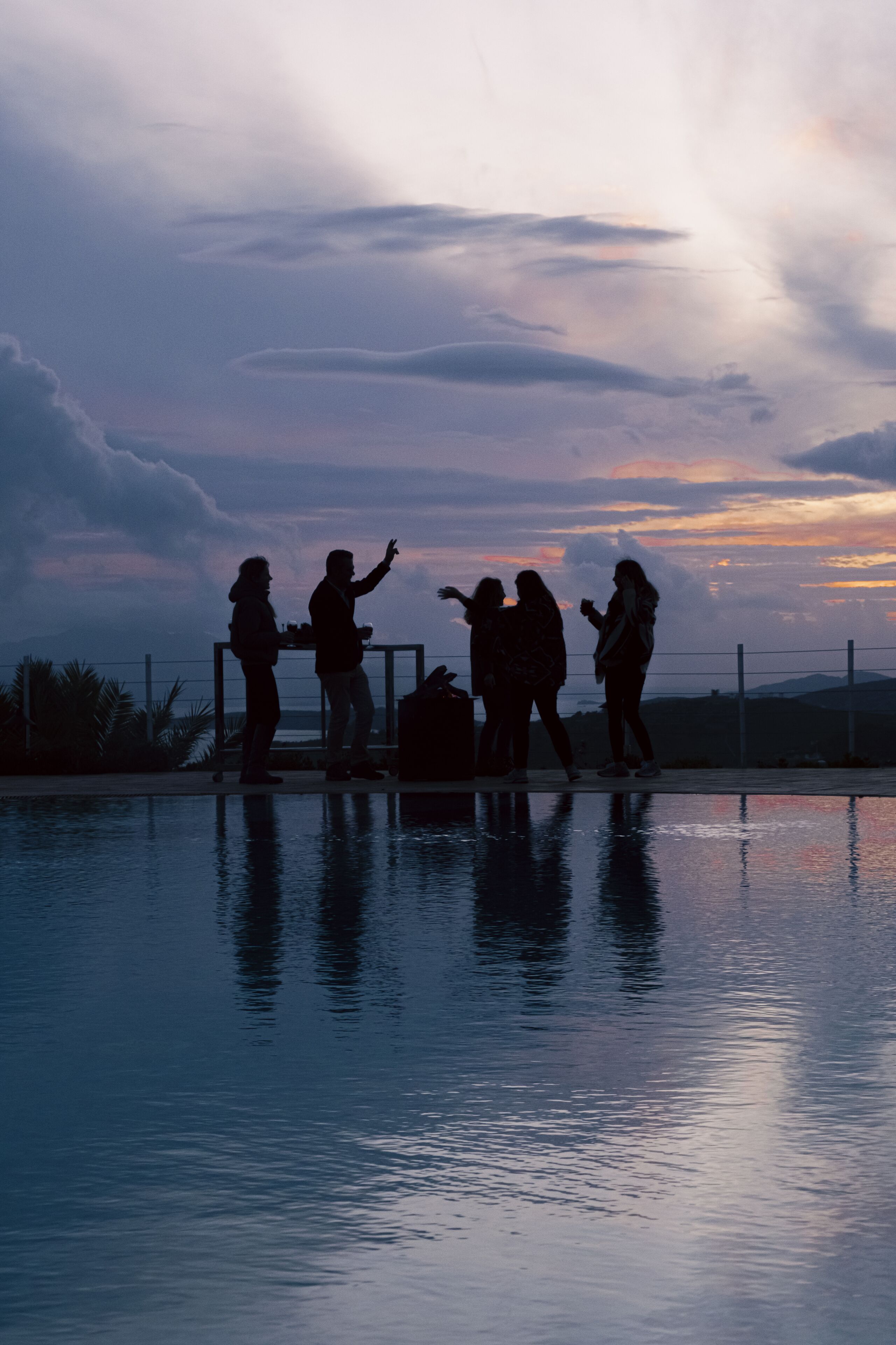 A group of people standing by a pool at sunset.