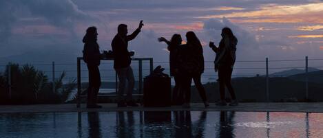 A group of people standing by a pool at sunset.