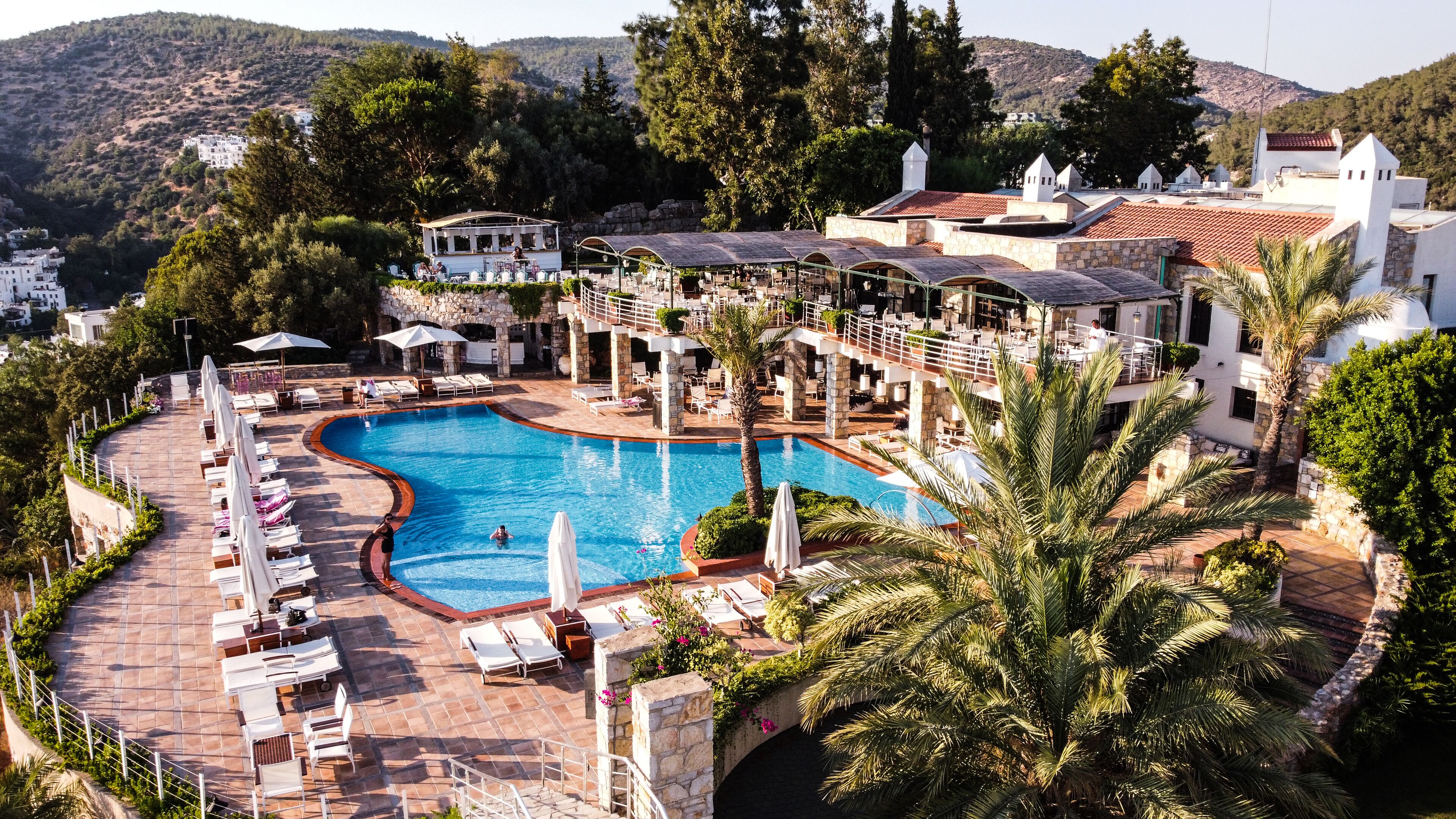 Un resort con una gran piscina, tumbonas y vistas de las colinas circundantes.