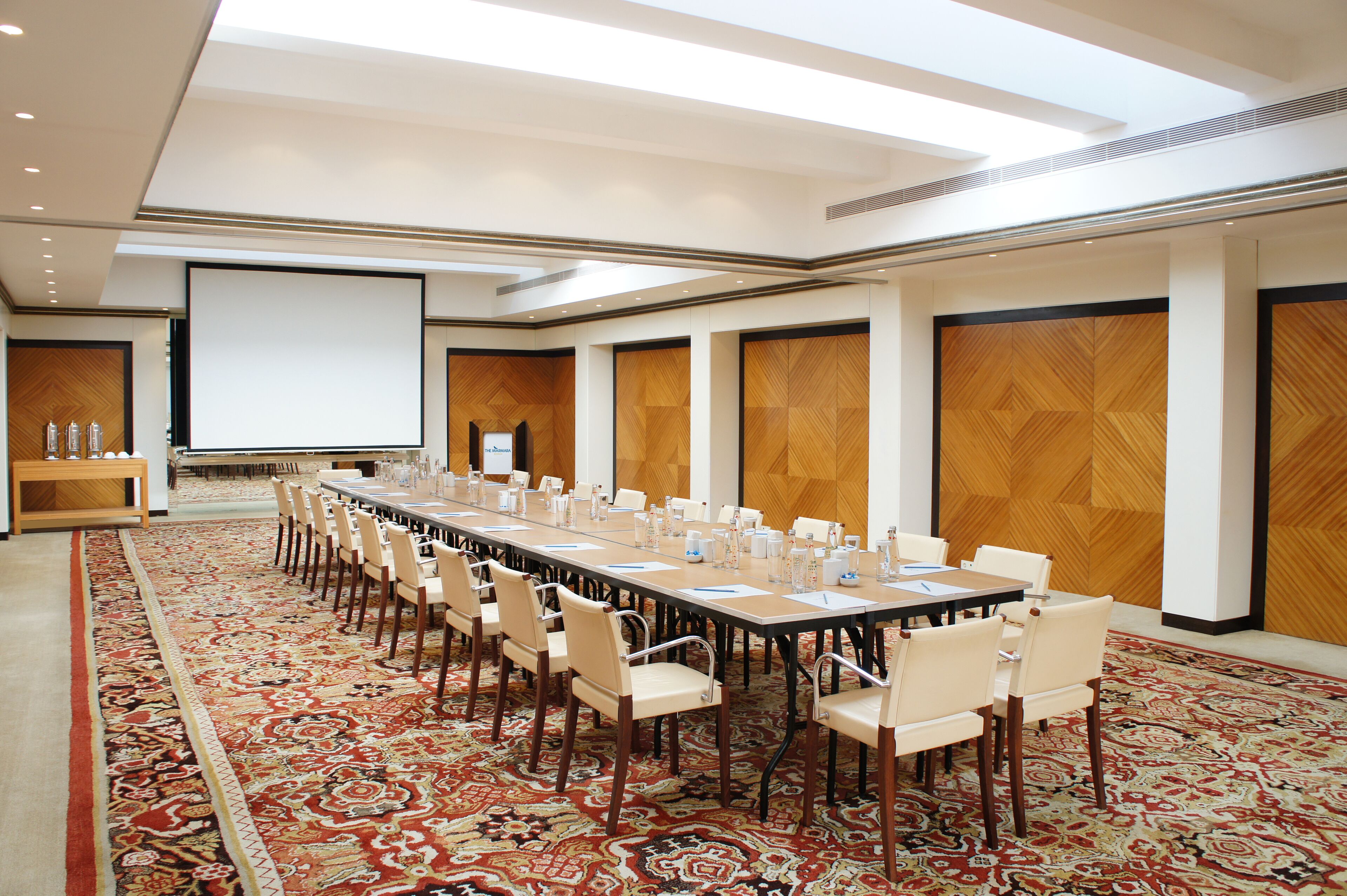 A conference room with a long table, chairs, a projector screen, and a carpeted floor.