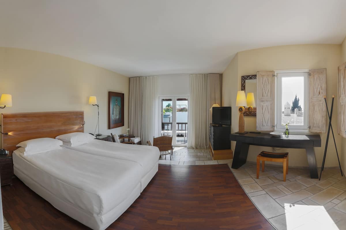 A hotel room with a large bed, a desk, a chair, a TV, and a window with curtains.
