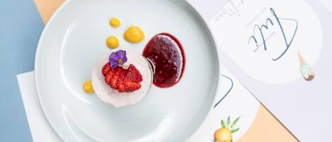 A dessert plate with a white plate, yellow dots, and a red sauce.