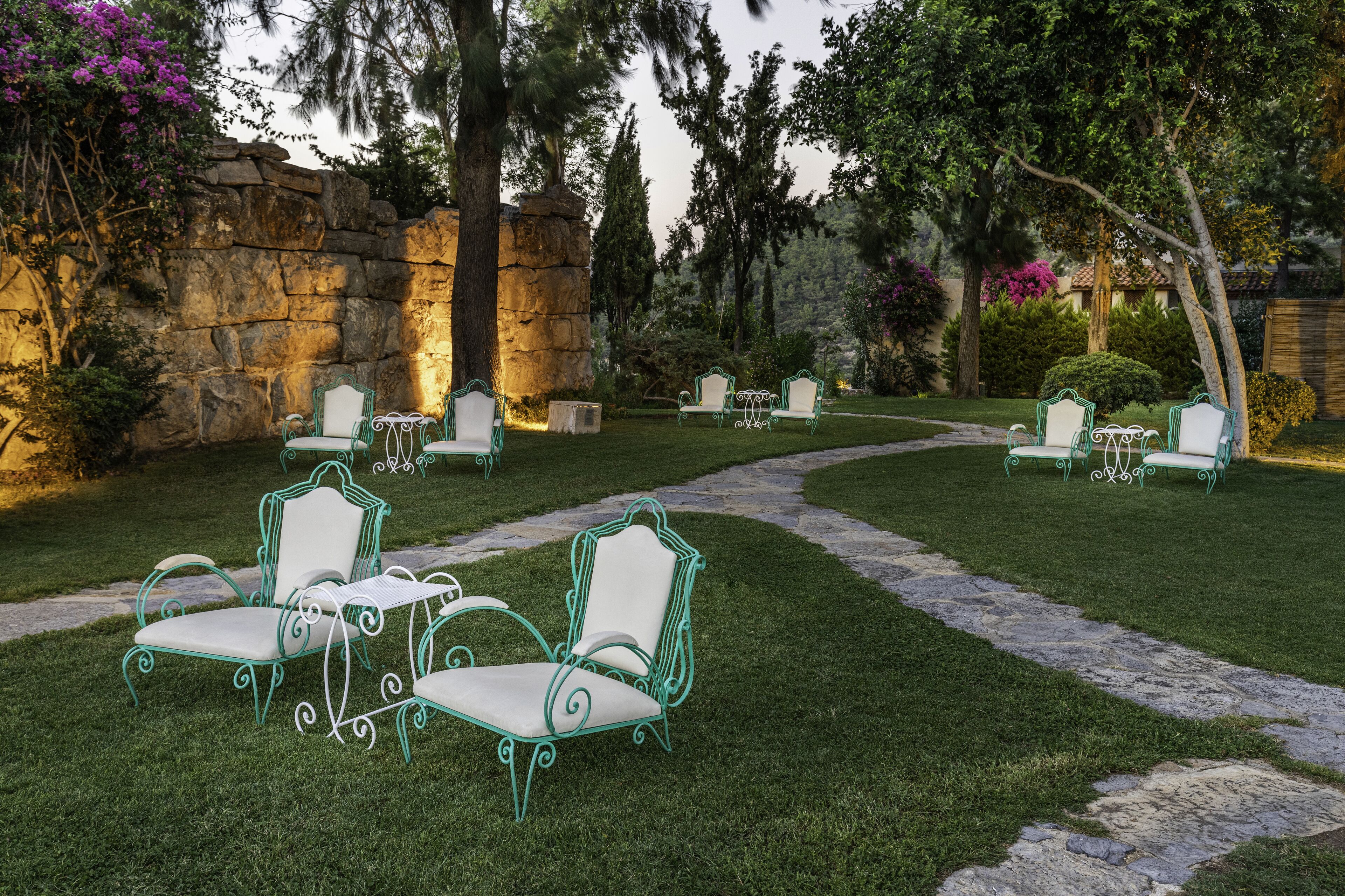 A garden with stone walls, green metal chairs, and a stone pathway.