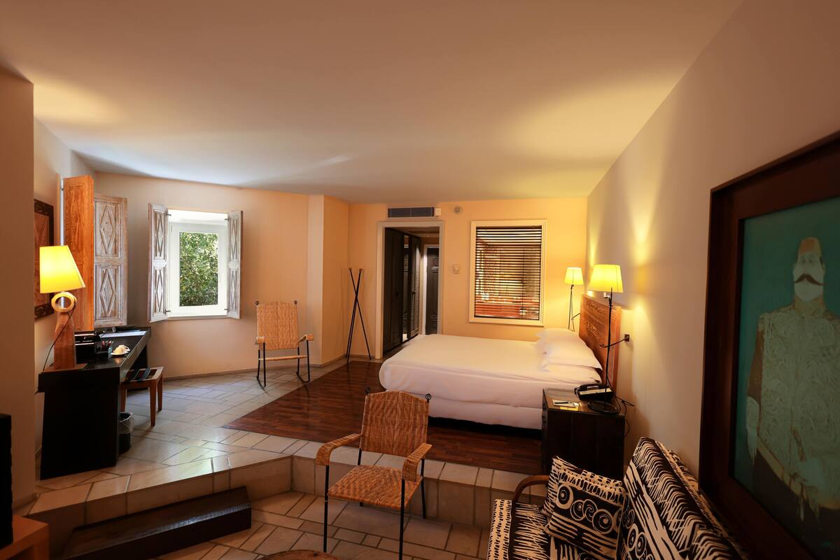 A hotel room with a bed, a desk, a chair, a sofa, and a painting on the wall.