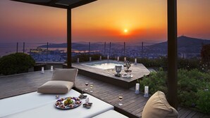 Eine Dachterrasse mit Whirlpool, Sitzgelegenheit und einem malerischen Sonnenuntergang.