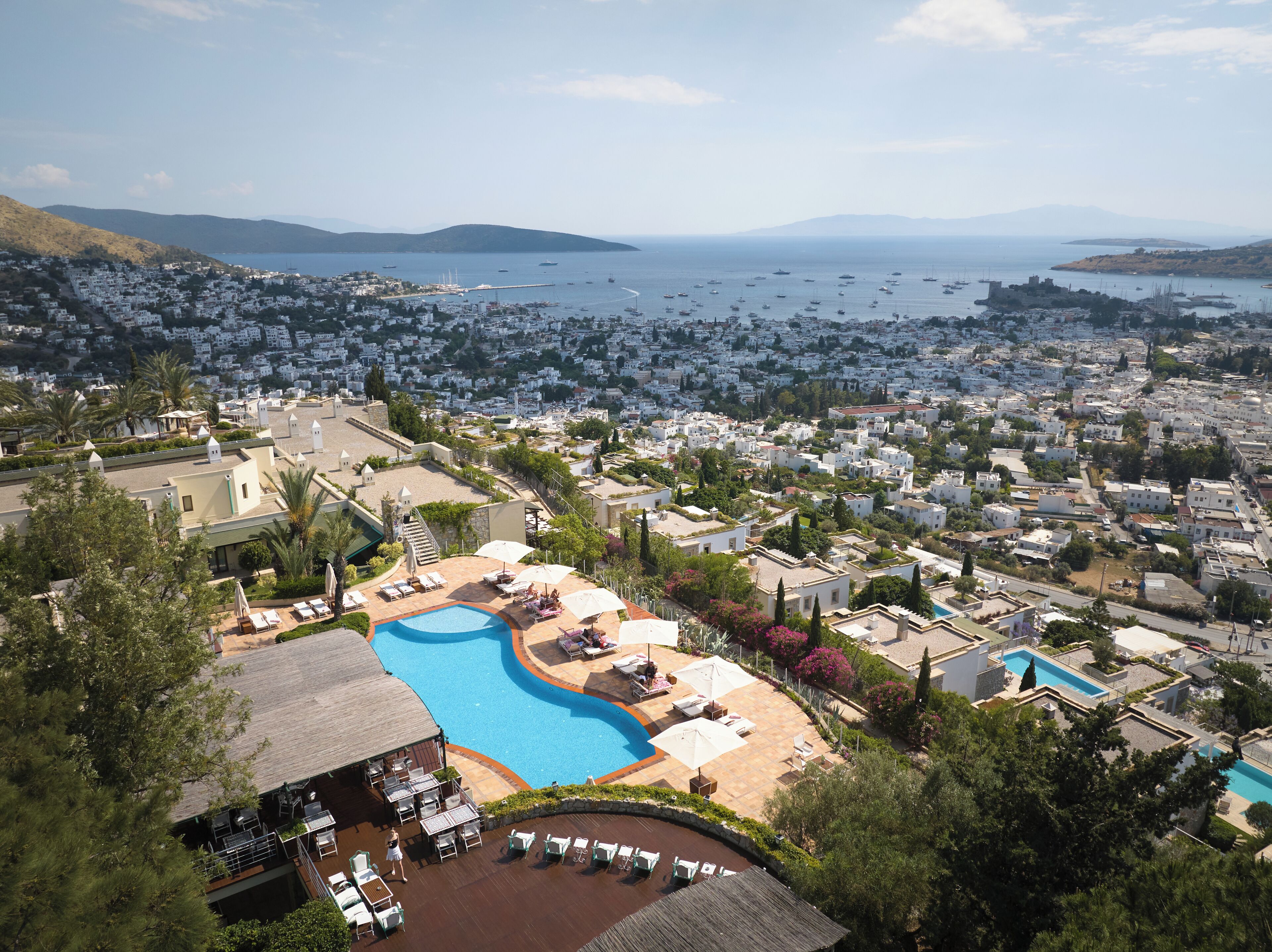 A resort with a swimming pool, lounge chairs, and a view of the sea and town.