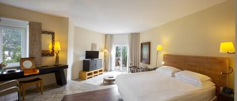 A hotel room with a bed, desk, chair, television, and a view of the outdoors.
