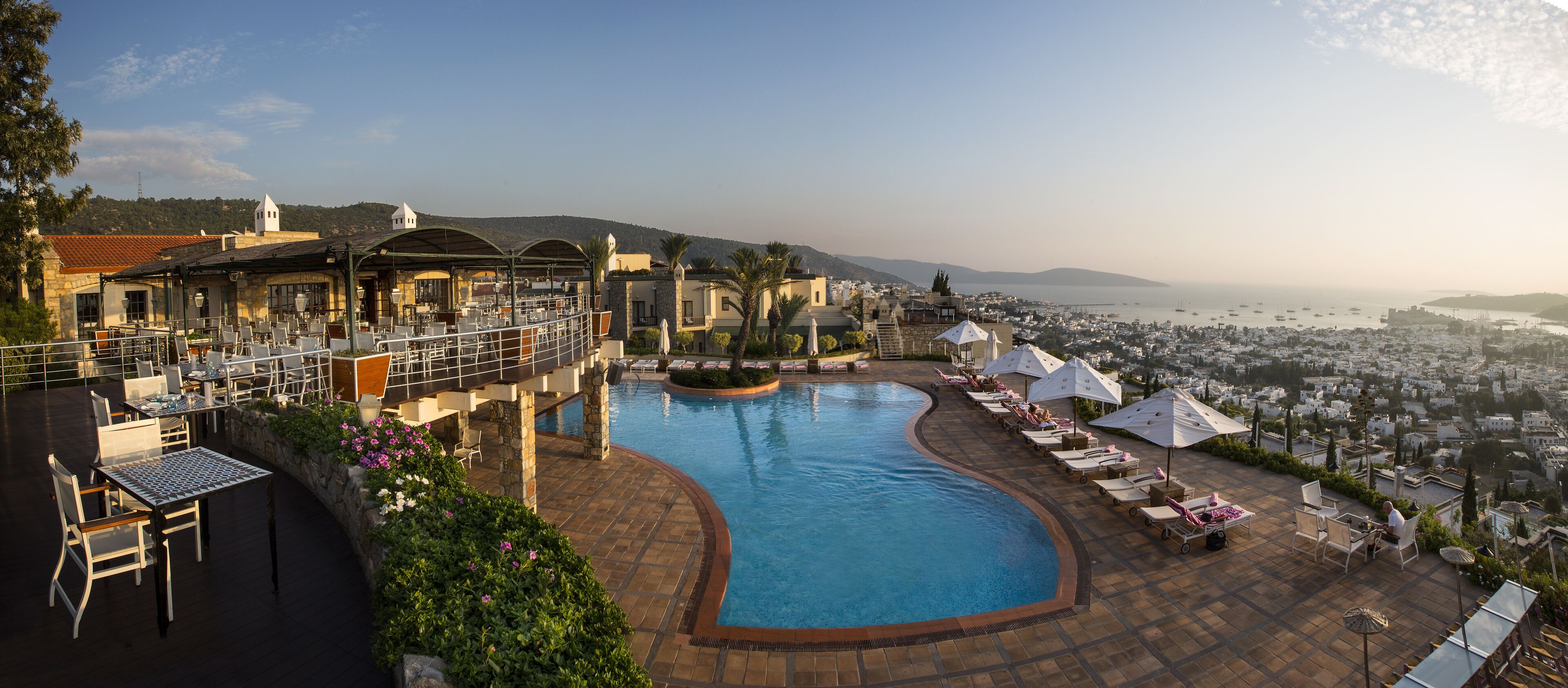A pool area with lounge chairs and a view of the city.