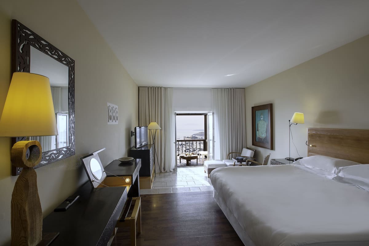A hotel room with a large bed, a desk with a lamp, a television, and a view of the outdoors.