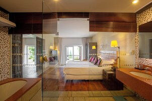Una habitación de hotel moderna con una cama grande, cabina de ducha de vidrio, baño independiente con lavamanos y vistas al exterior.