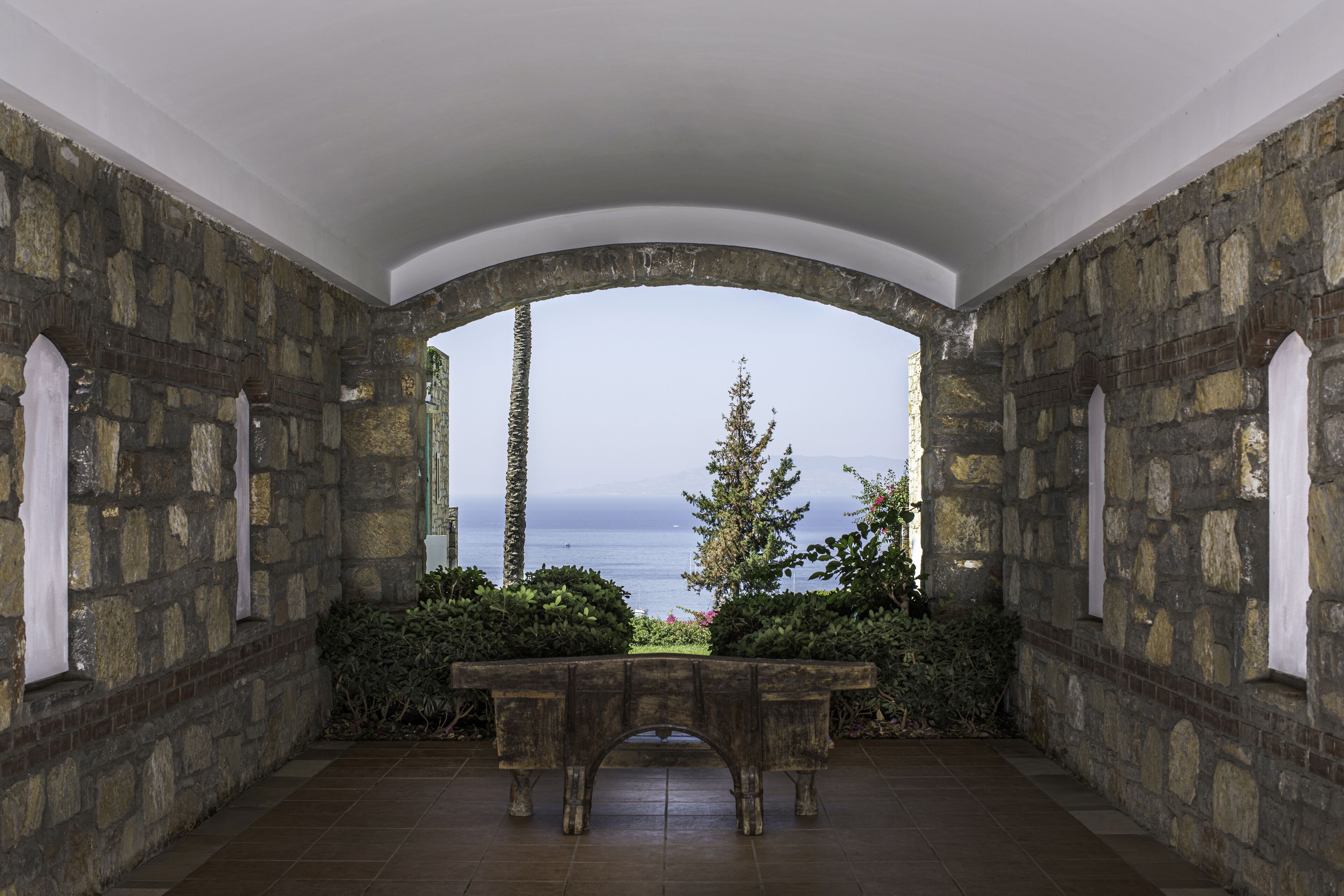 Una habitación de paredes de piedra con una banca y vistas al mar.