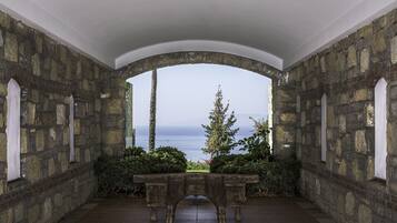 Una habitación de paredes de piedra con una banca y vistas al mar.