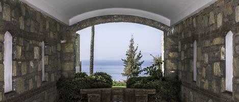 Una habitación de paredes de piedra con una banca y vistas al mar.