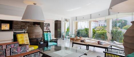 A spacious living area with a large glass table, colorful patterned sofas, and a stone fireplace.