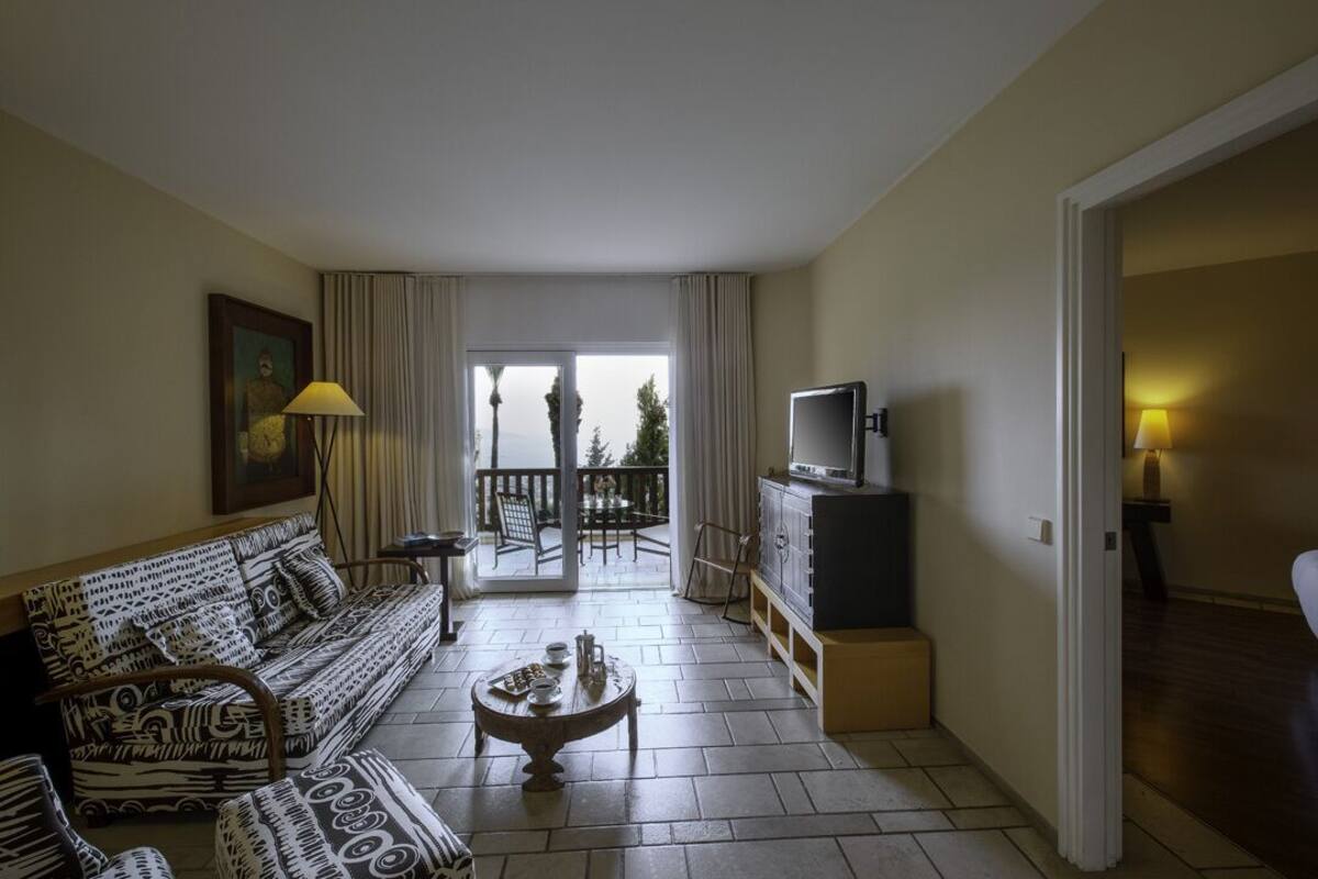 A living room with a sofa, a coffee table, a TV, and a balcony with a view.