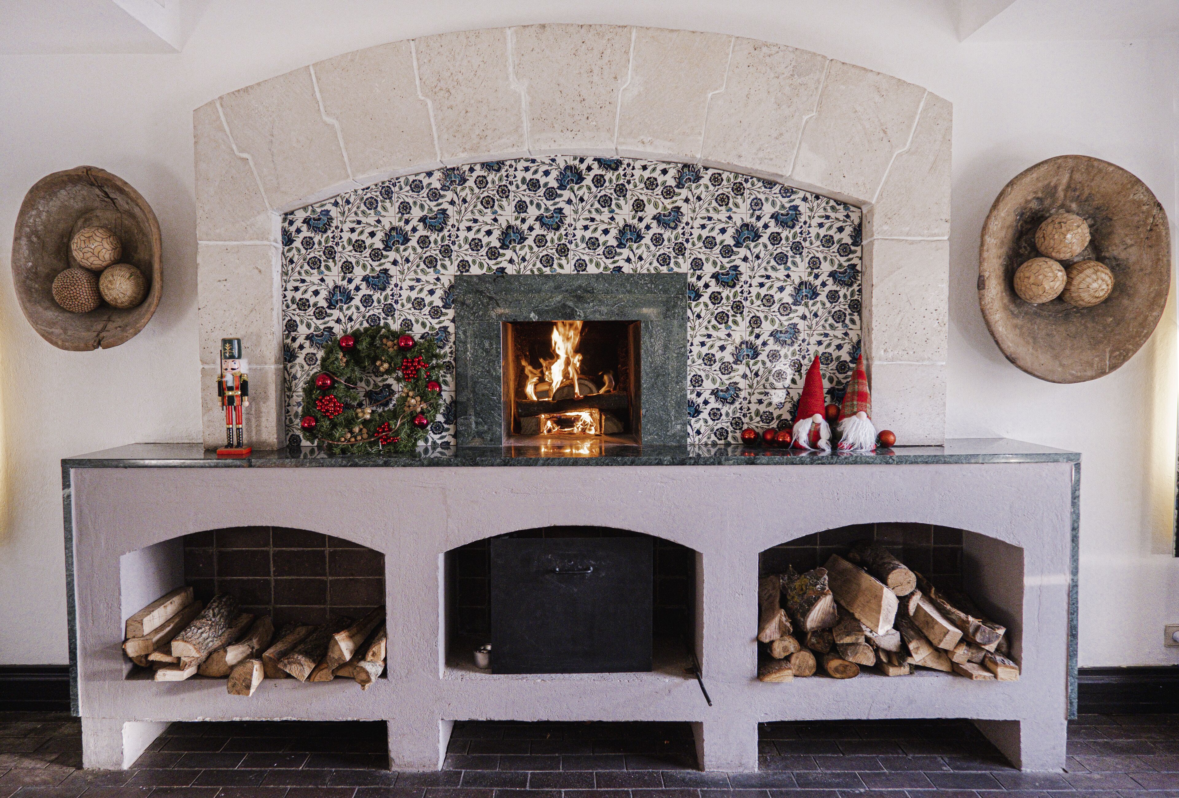A fireplace with a tiled surround, a mantel with decorations, and logs stored in the lower section.