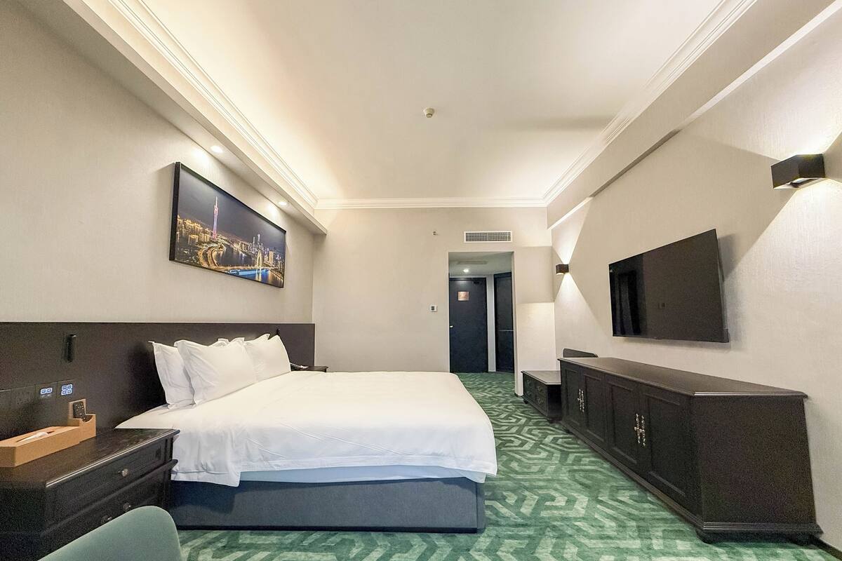 Een hotelkamer met een bed, een bureau, een televisie en een schilderij aan de muur.