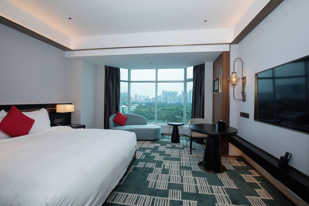 Een hotelkamer met een groot bed, een zithoek, een televisie en uitzicht op de stad.