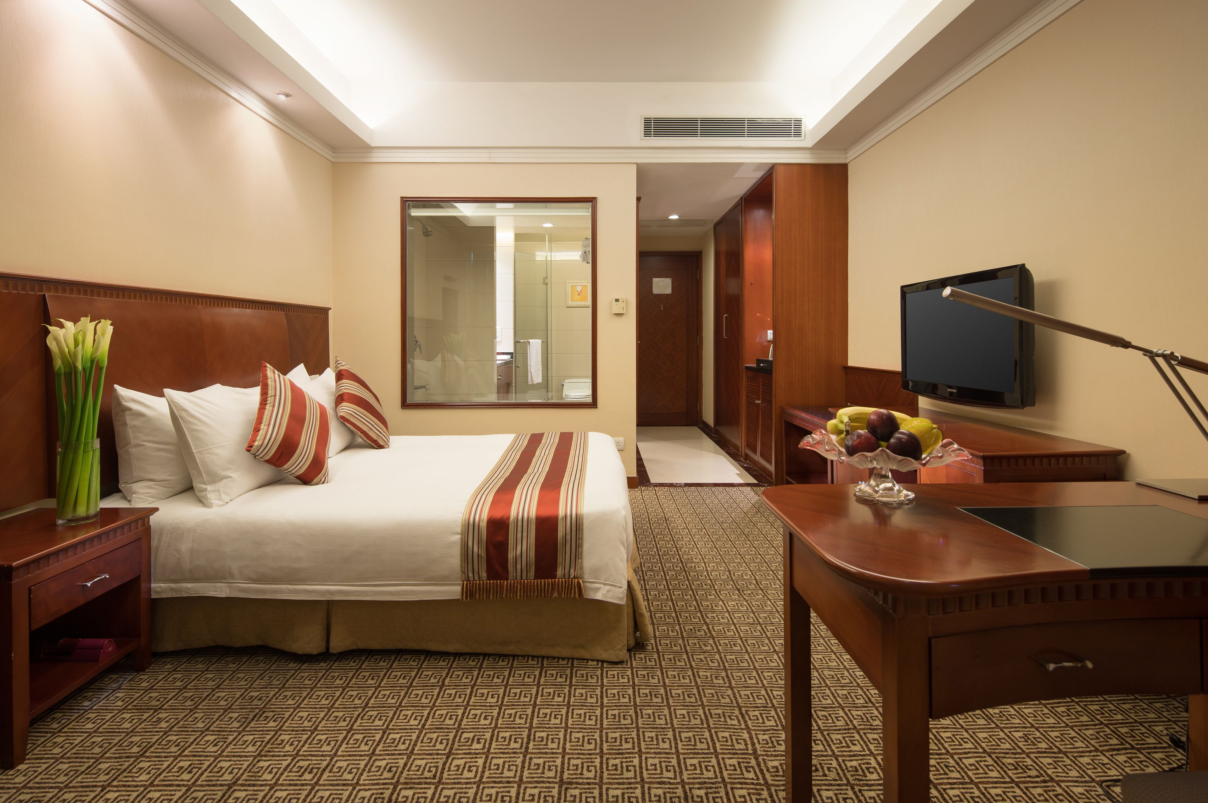 A hotel room with a bed, bedside table, TV, desk, and a mirror.