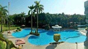 Un resort con varias piscinas, palmeras y una torre al fondo.