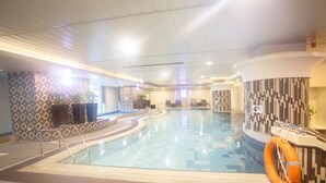 Una piscina interior con suelo de baldosas, un flotador salvavidas y una zona de estar con sillas.