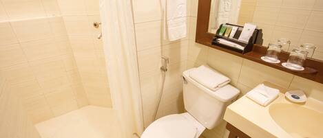 A bathroom with a shower, toilet, sink, and a mirror with toiletries.