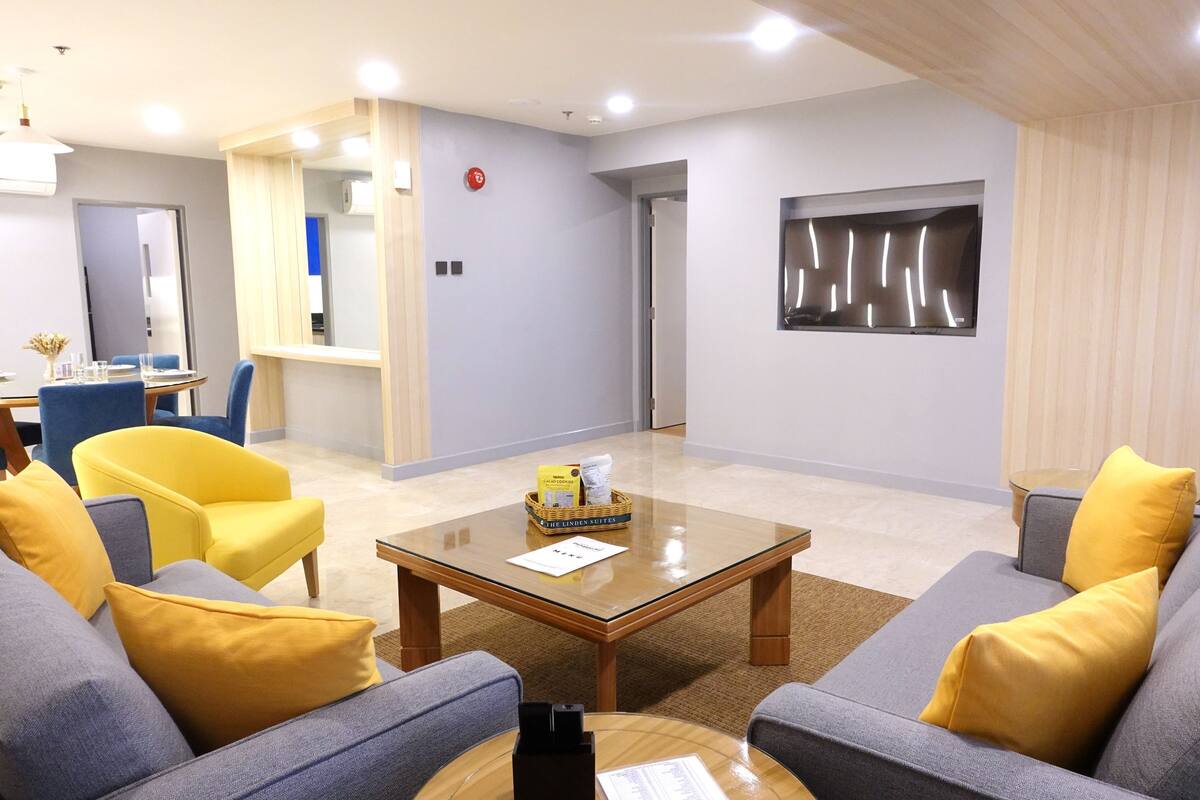 A modern living room with a glass coffee table, two sofas with yellow cushions, a blue armchair, and a small side table with a basket.
