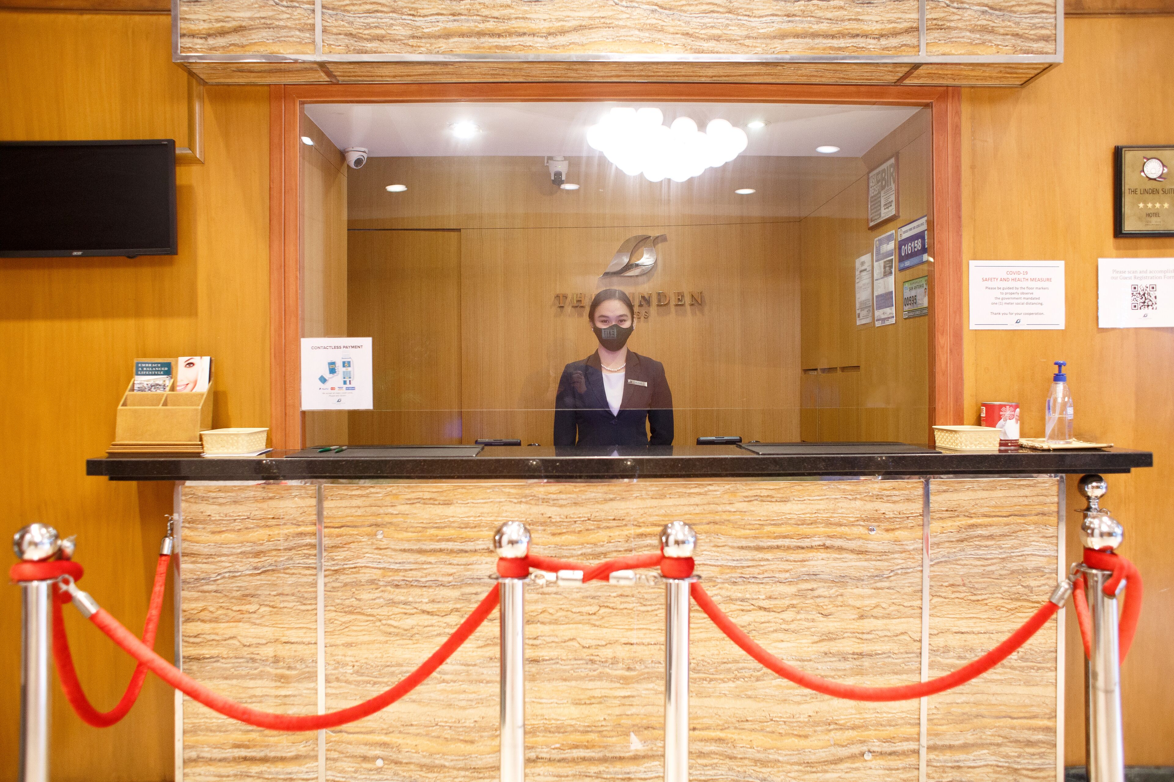 A hotel reception desk with a wooden panel design, a nameplate, and a security camera.
