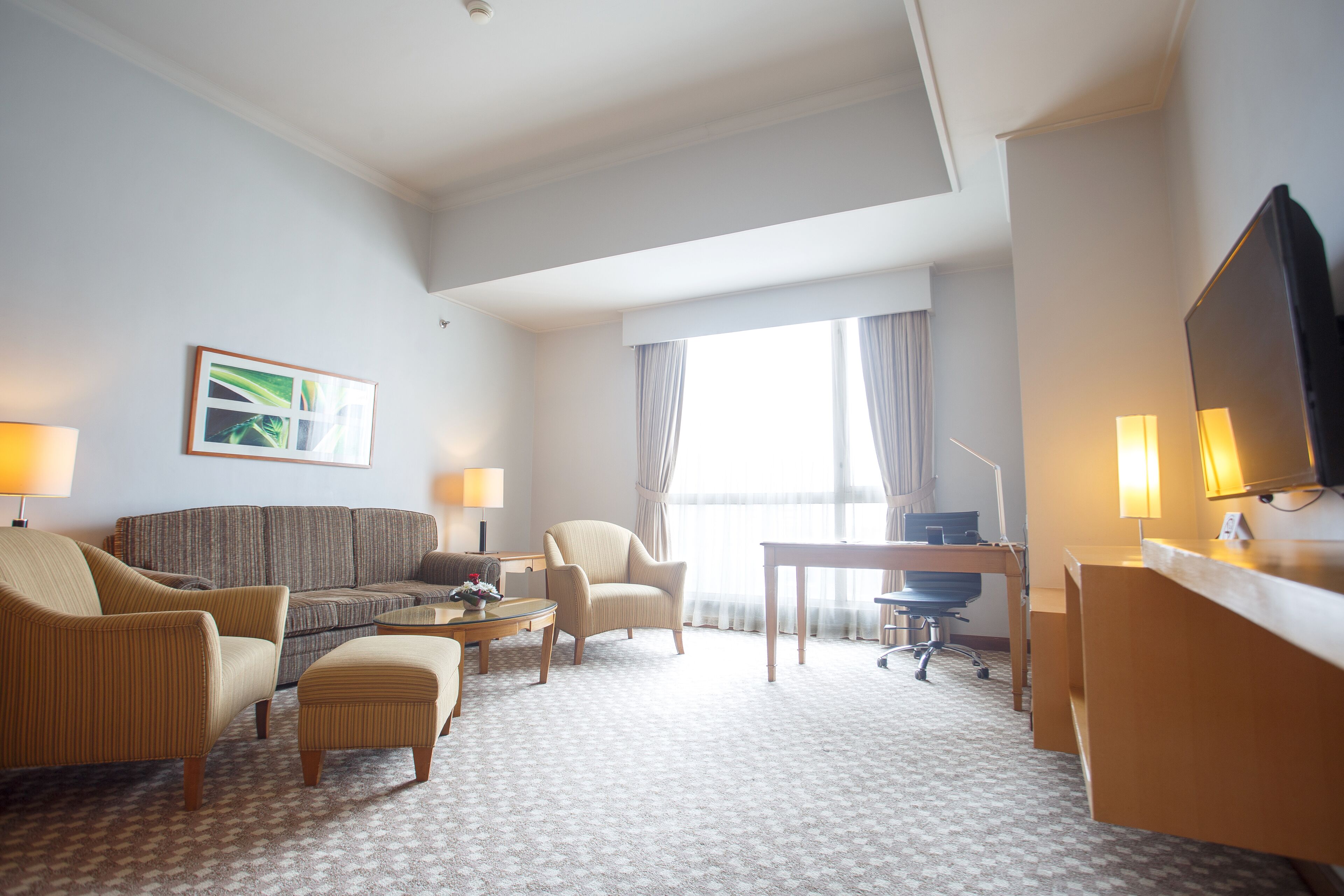 A hotel room with a sofa, armchairs, a small table, a desk, and a television.