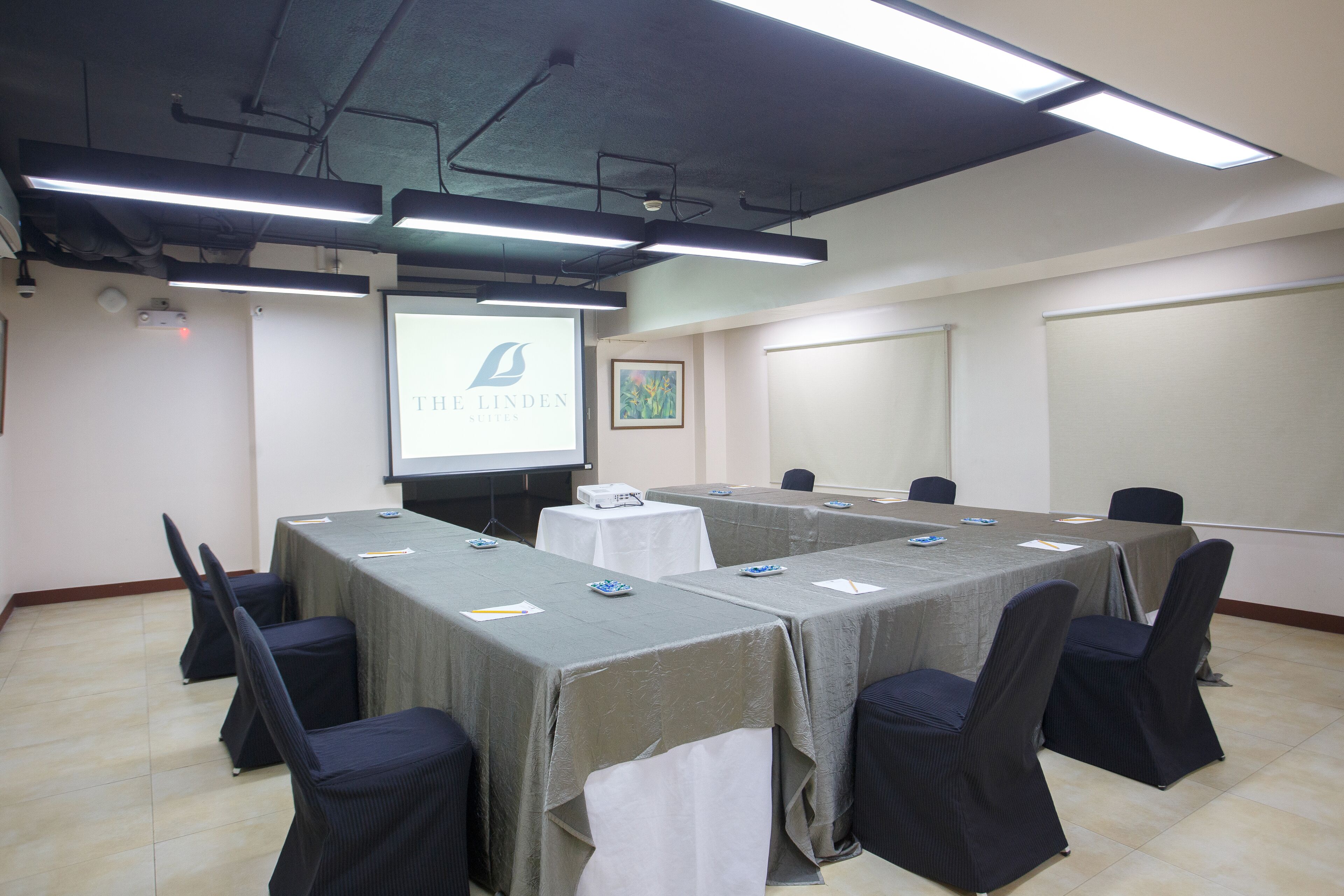 Un salón de conferencias con una larga mesa, sillas, una pantalla de proyector y una pantalla para presentaciones.