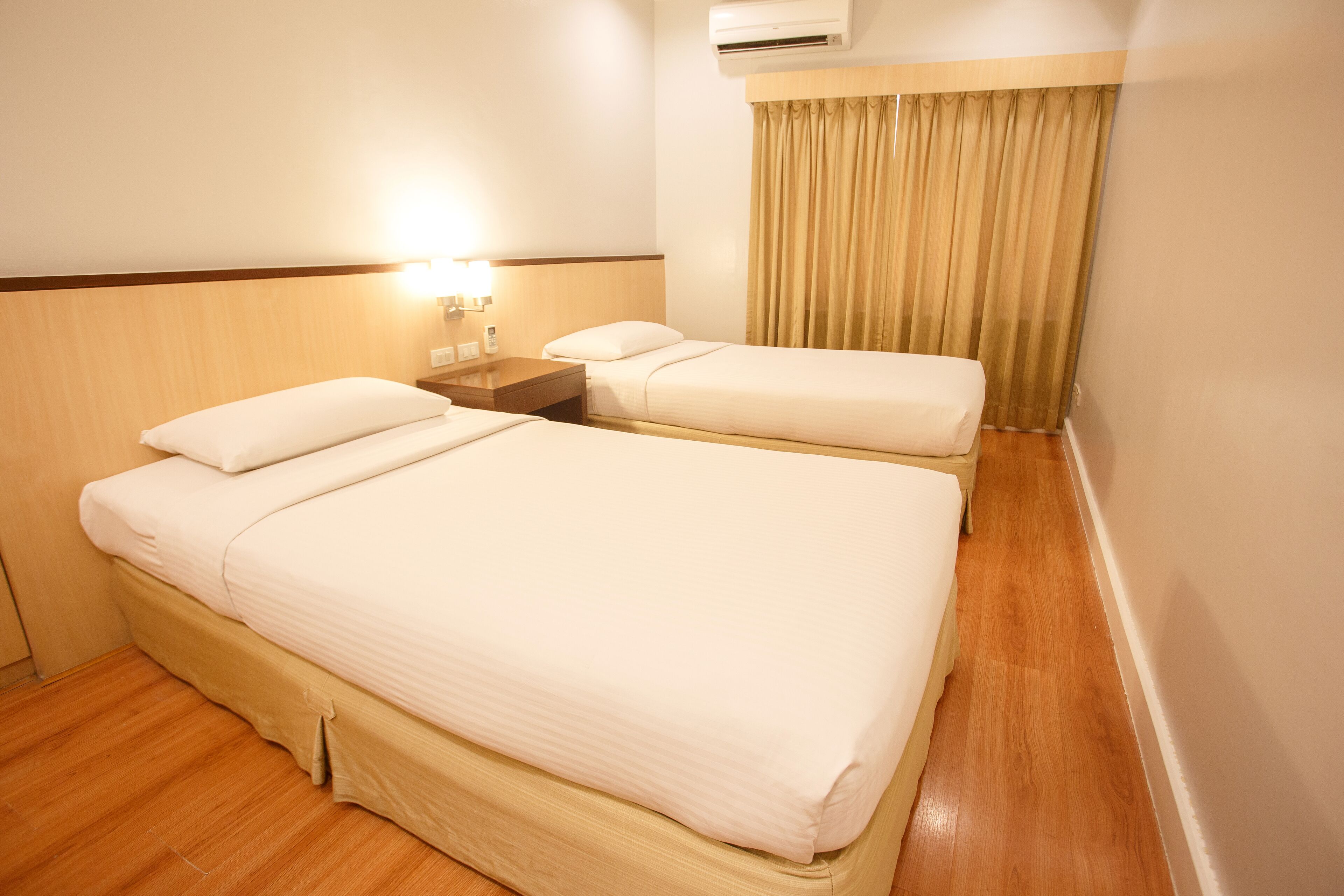 A hotel room with two beds, a nightstand, an air conditioning unit, and a curtain.