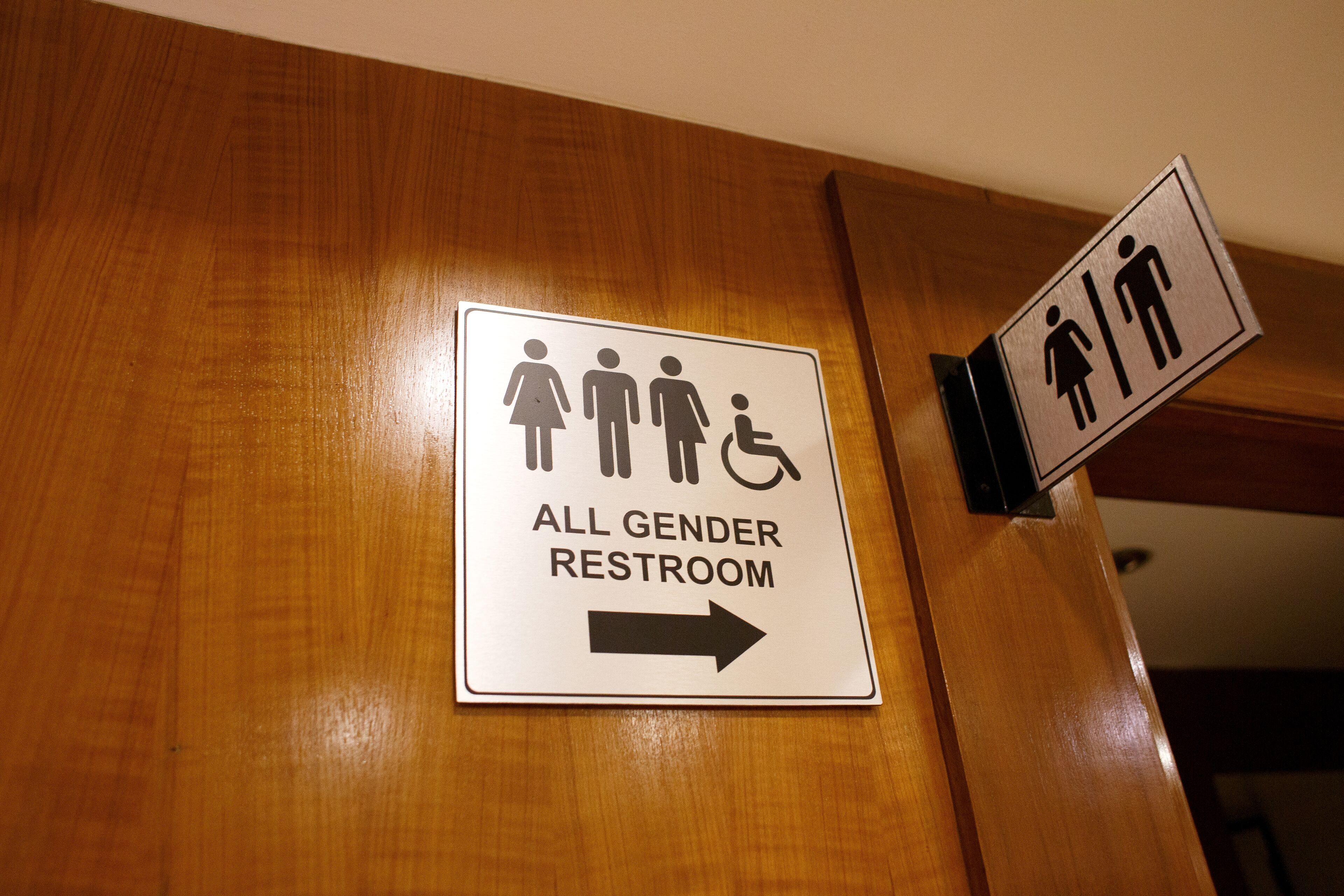 A sign indicating an all gender restroom with a directional arrow.