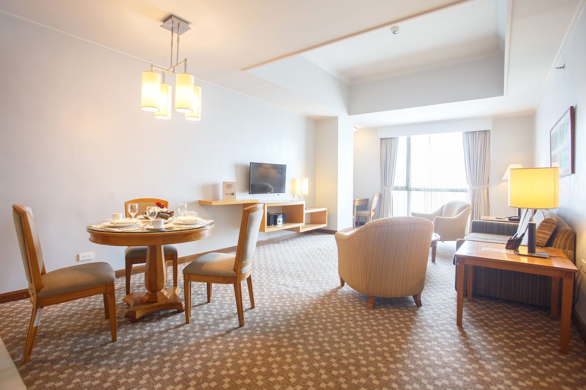 A hotel room with a dining area, a TV, a sofa, and a lamp.