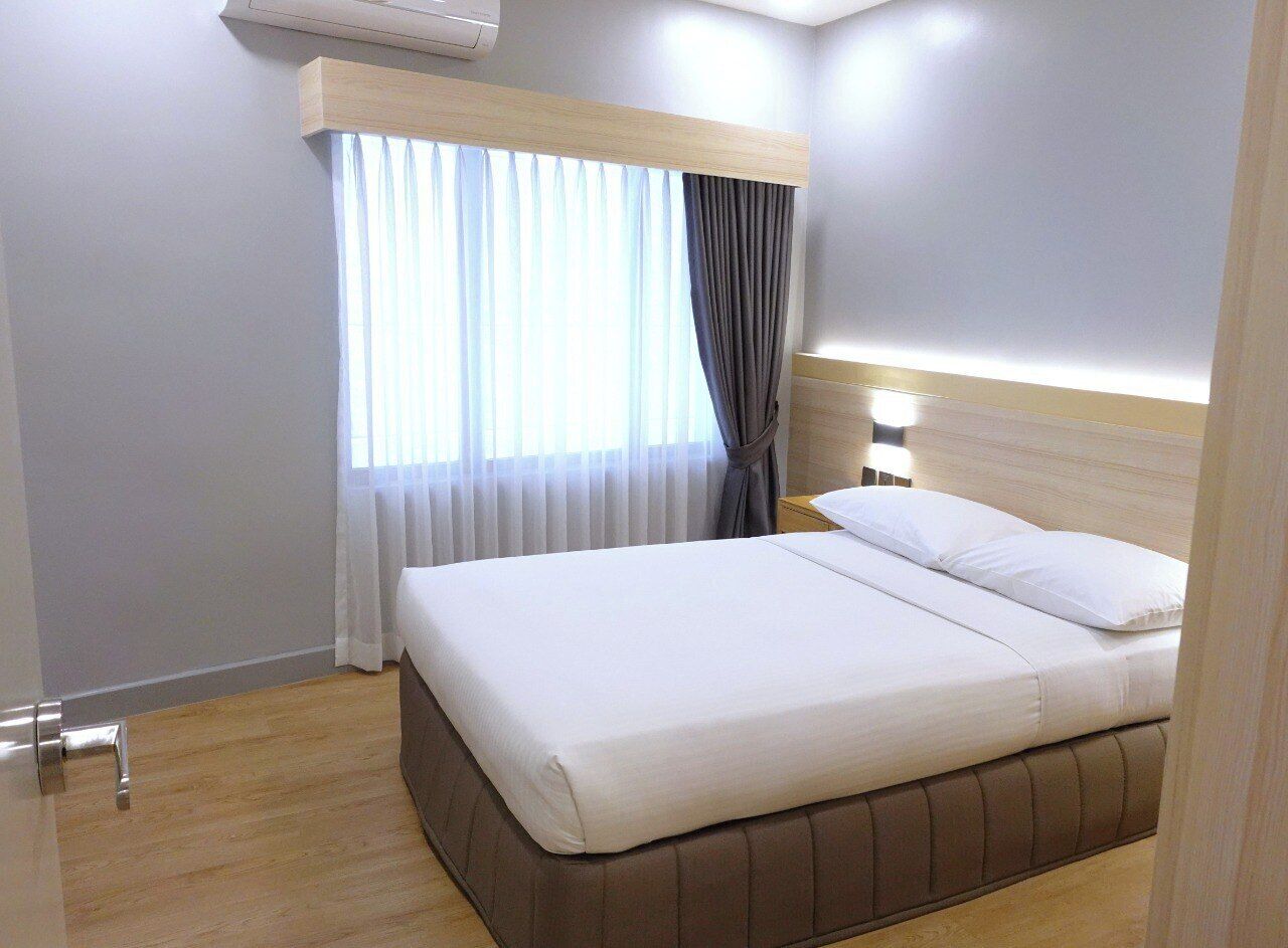 Una cama bien hecha en una habitación de hotel con cabecera de madera, una ventana con cortinas y un aire acondicionado de pared.