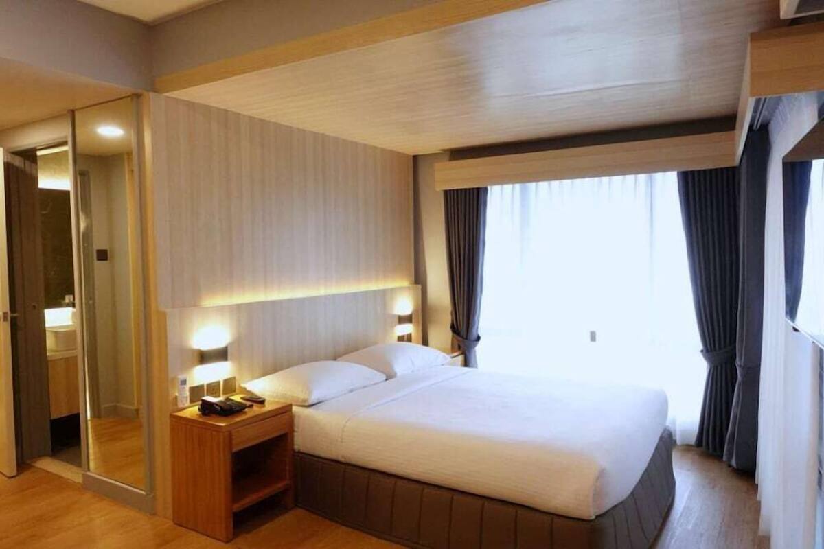 A hotel room with a bed, bedside lamps, a mirror, and a window with curtains.