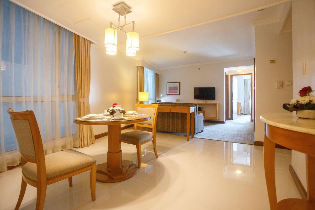 A hotel room with a dining area, a TV, and a view of the hallway.
