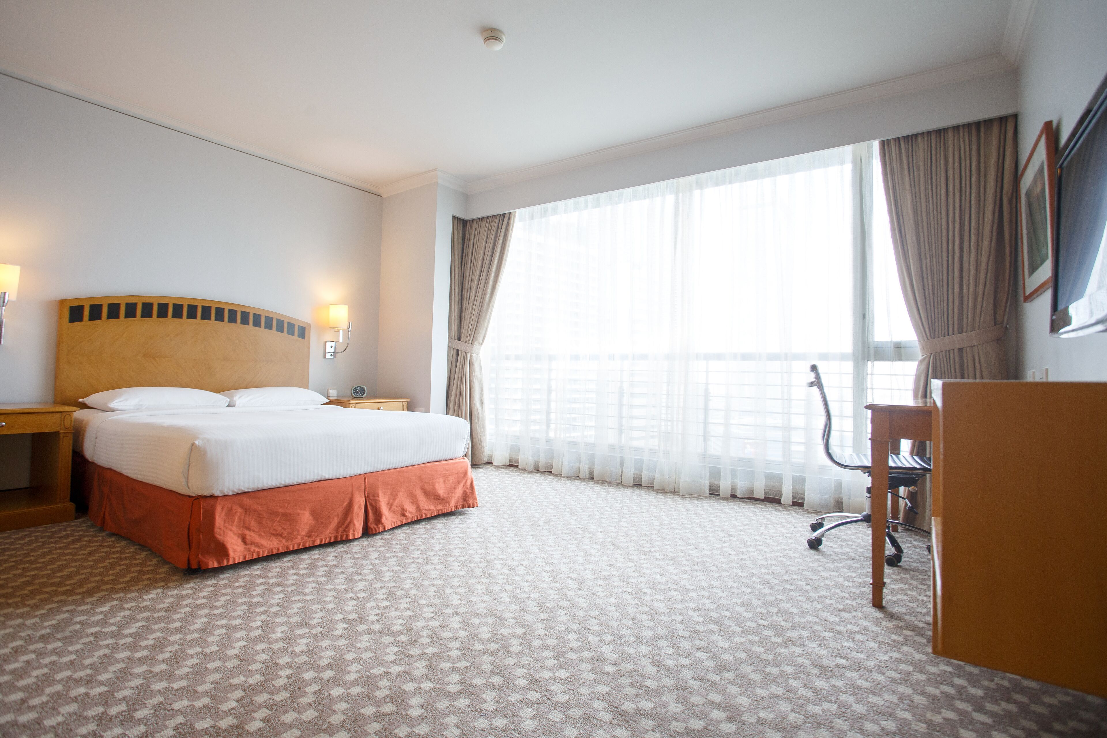 Quarto de hotel com uma cama grande, uma escrivaninha e uma cadeira.
