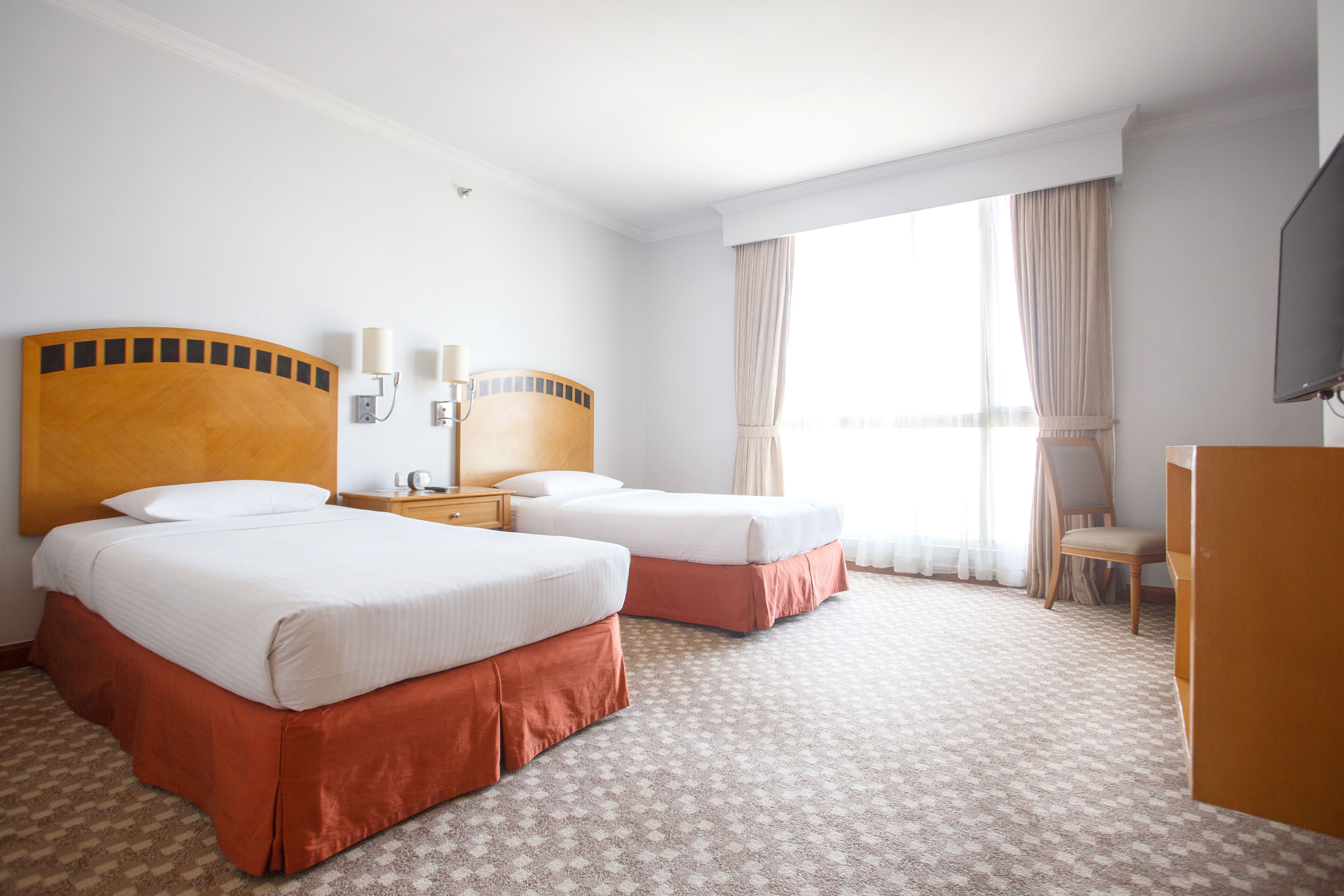 Ett hotellrum med två sängar, ett skrivbord, en stol och en tv.